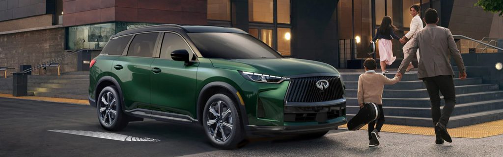 Green INFINITI SUV parked outside a modern building as a family walks toward the entrance.