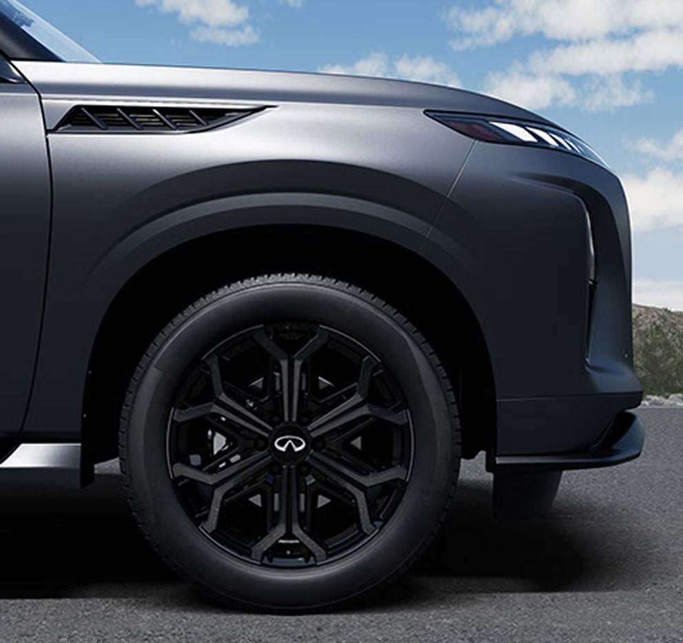 Close-up of the front right wheel and fender of a matte black Infiniti SUV, featuring distinctive black rims.