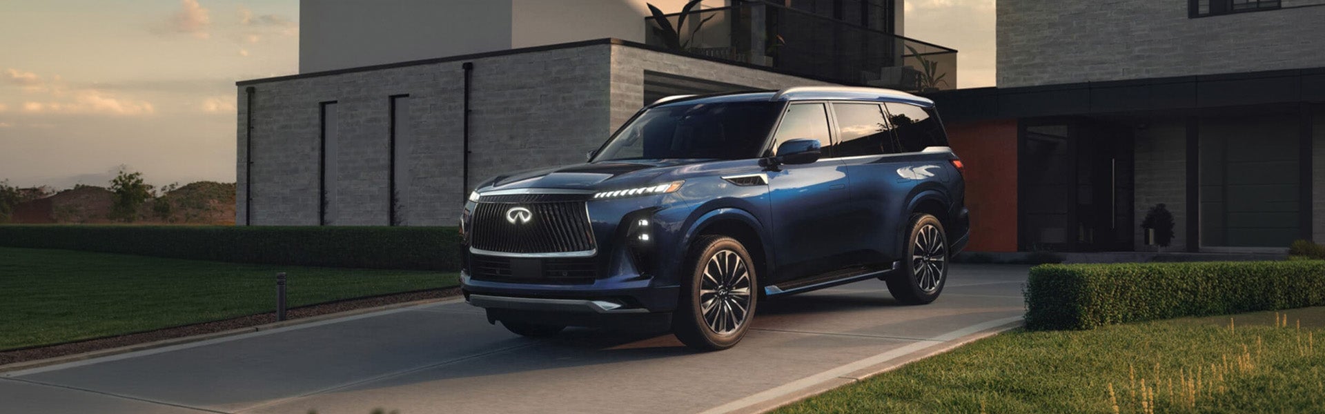 Blue INFINITI SUV parked outside a modern home during sunset with landscaped surroundings.