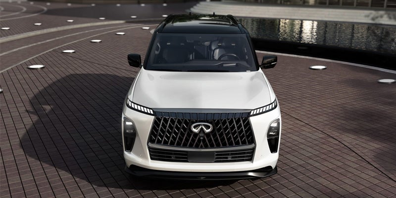 Front view of a white INFINITI QX80 SUV with a black roof parked on a modern paved surface.