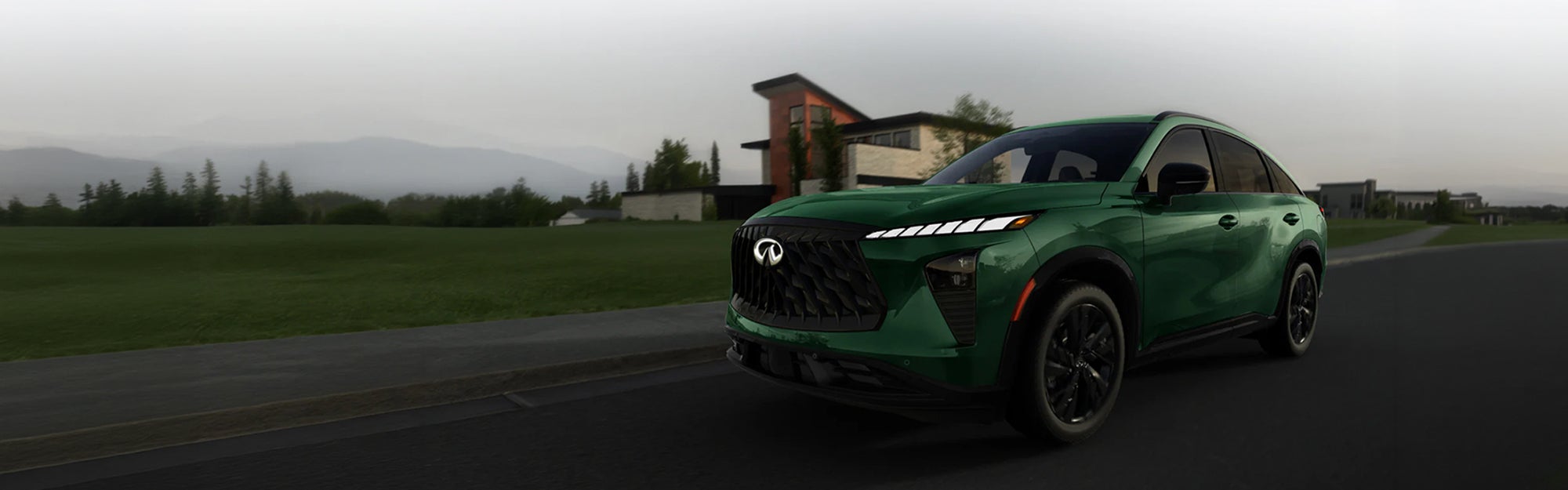 Green INFINITI SUV driving on a road with a modern home and mountains in the background.