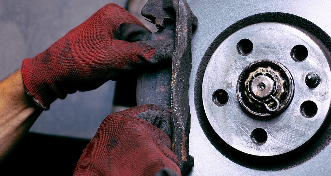 Brake technician inspecting a vehicle brake pad and rotor assembly during brake service.